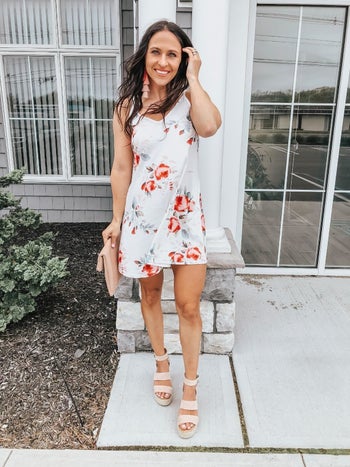 a reviewer wearing the tank dress in white with a red floral print 