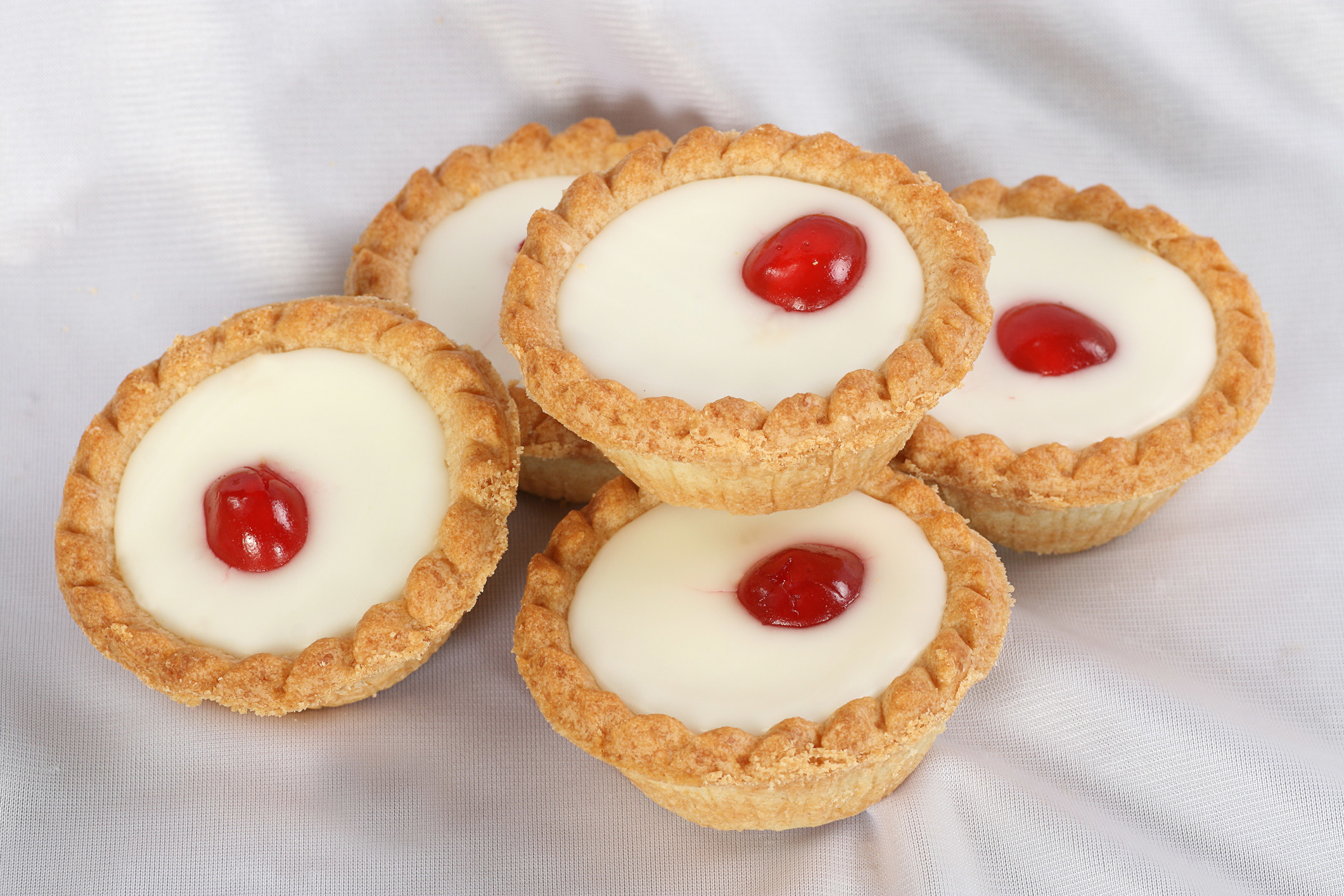 A stack of tiny tarts with a layer of frangipane and a cherry in the middle.