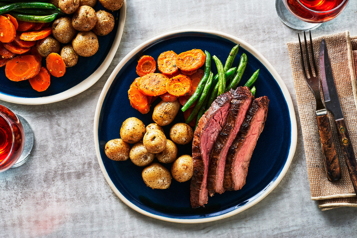 A plate with carved flank steak, green beans, roasted little potatoes, and sliced carrots.