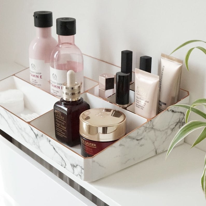 a white marble makeup holder with rose gold trim on the edges on a counter 