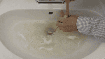 A person unclogging a sink with the drain snake and pulling out a clump of hair 