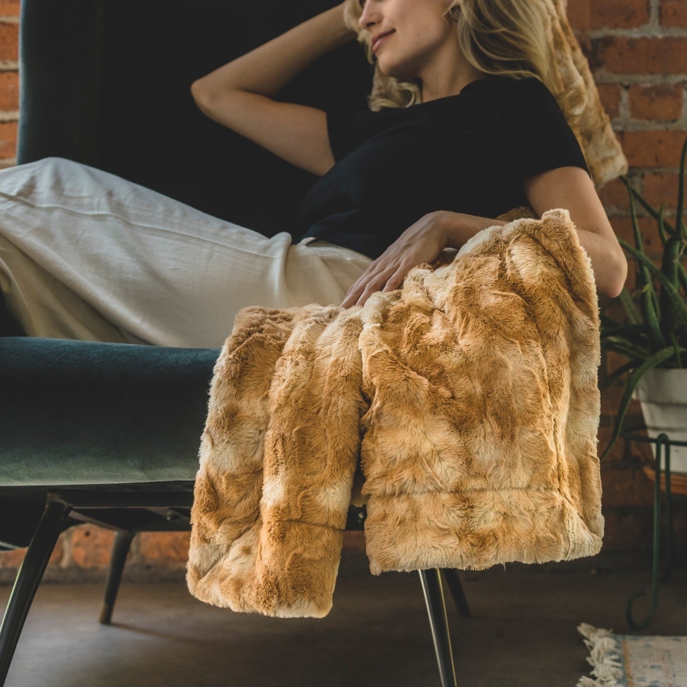 a model posing with the honey-brown colored faux fur sherpa throw on a chair 
