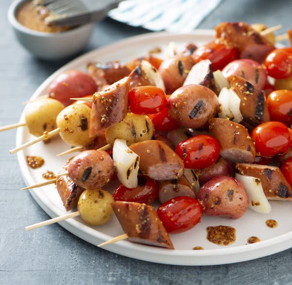 Bratwurst, little potatoes, and cherry tomato skewers piled onto a plate.
