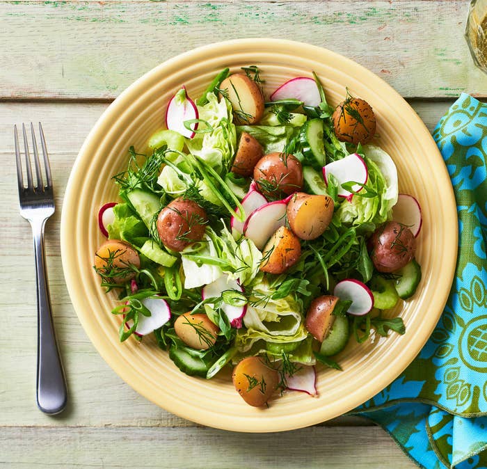 A bowl of mixed green salad with chopped radishes and little potatoes, garnished with dill.