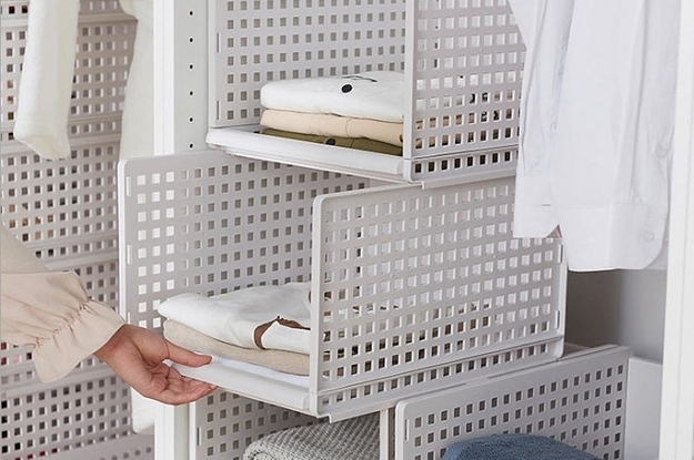 a hand reaching towards four white storage boxes stacked on top of each other, the boxes are holding towels, blankets, and clothing