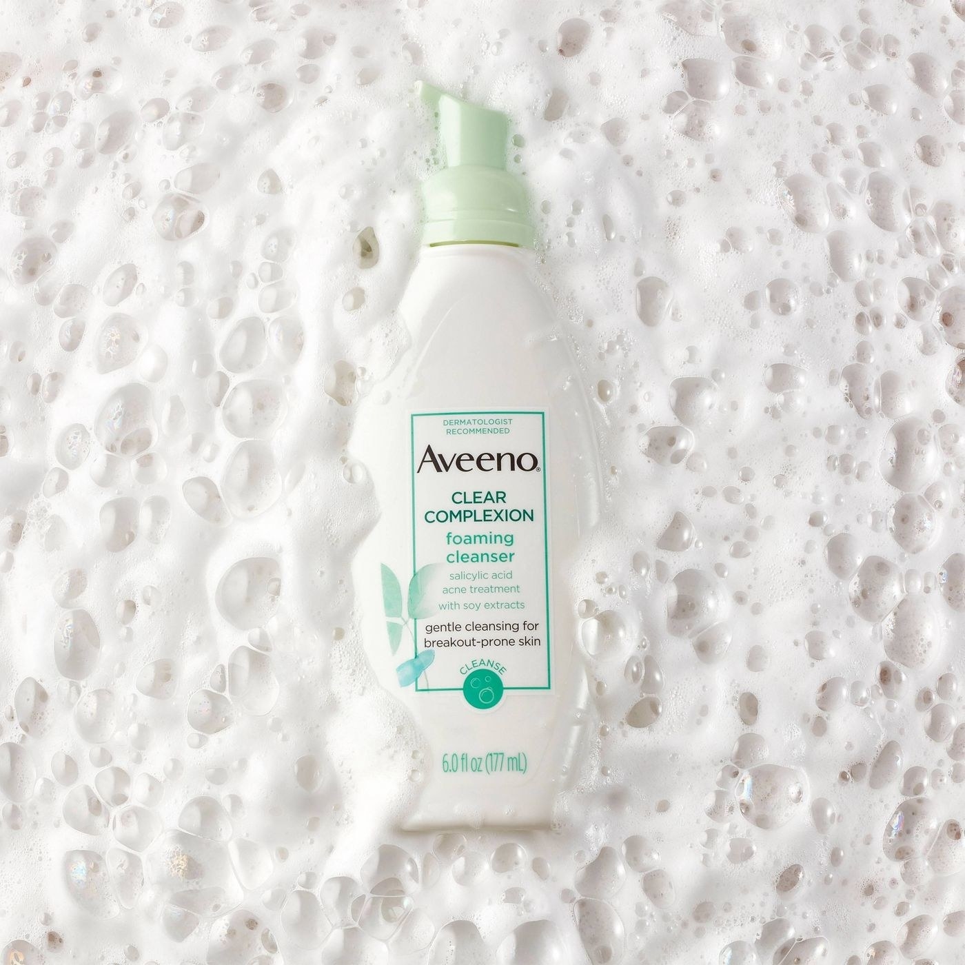 A bottle of foaming facial cleanser in a pile of soap suds