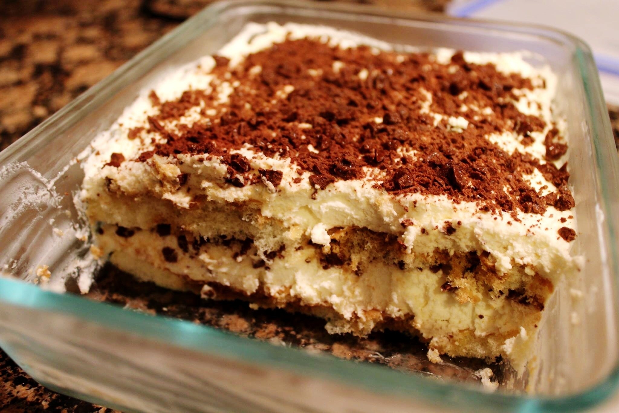 A glass container holds creamy, layered tiramisu with about 1/3 of the dessert gone