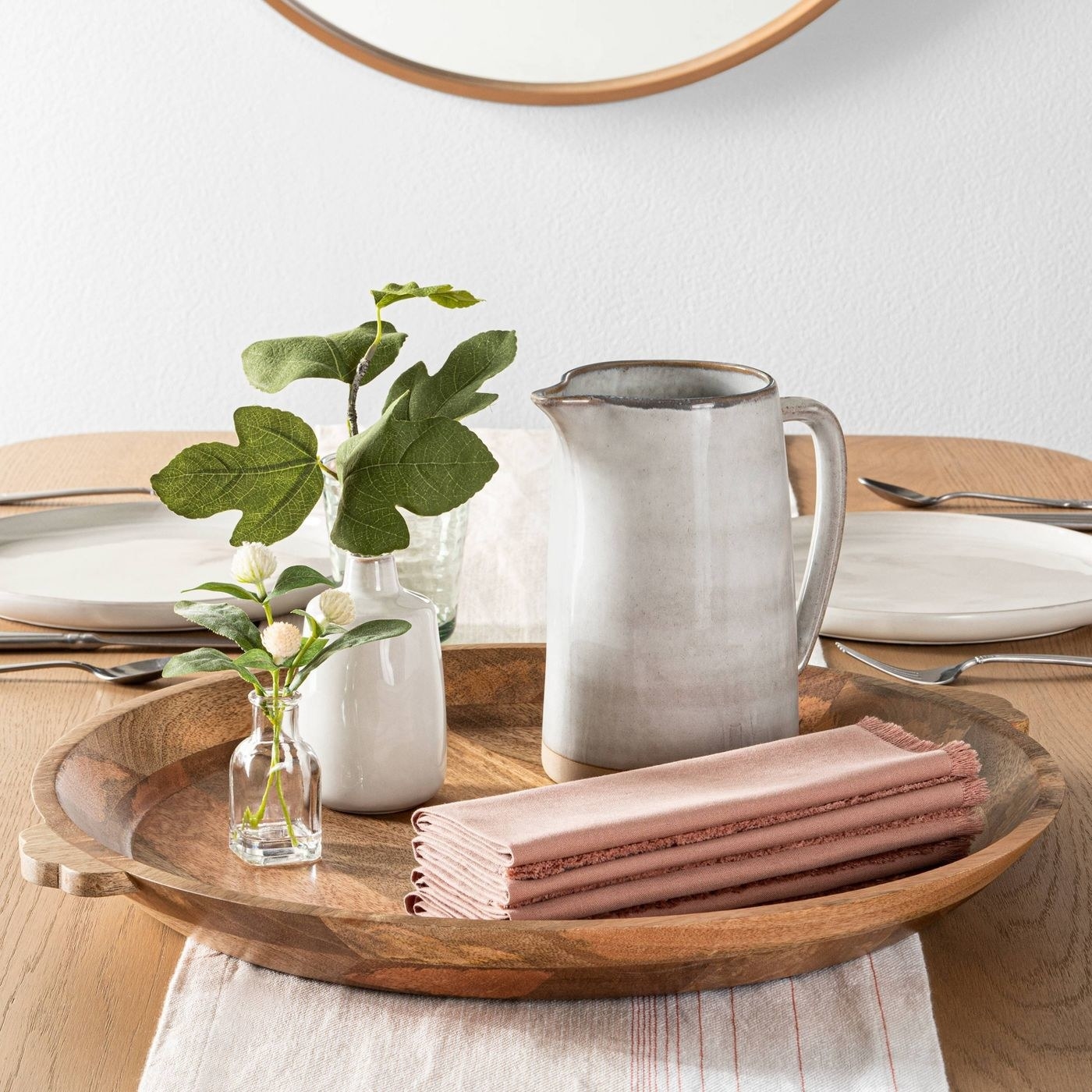 round wood tray with plants, a pitcher, and napkins on top, sitting on a table