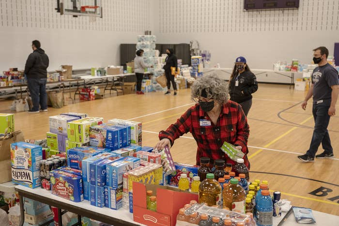 Folding tables in a school gymnasium are covered with boxes of fruit juice, Gatorade, and other food supplies