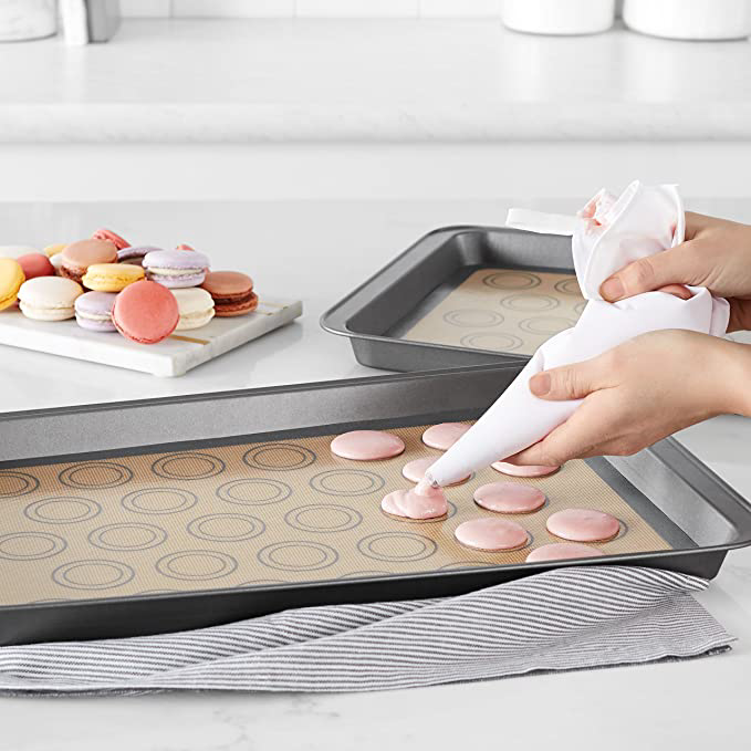 A person piping macarons on the sheet. It has circular markings for precision.