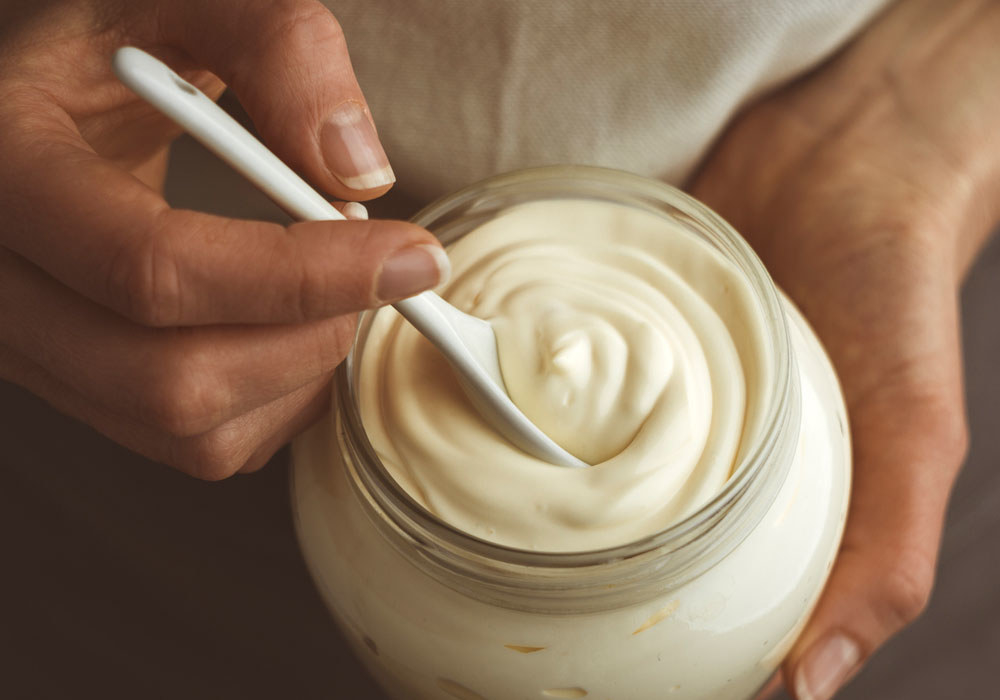A large tub of mayo with a spoon in it.