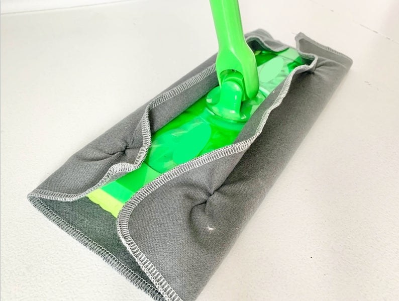 A Swiffer mop with on of the gray reusable covers on it 
