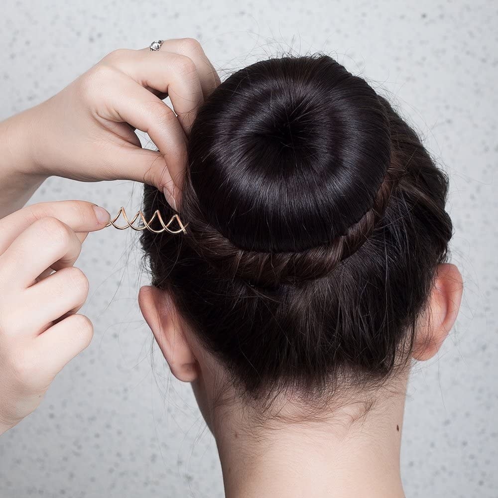 A person securing their hair bun with a spirally bobby pin
