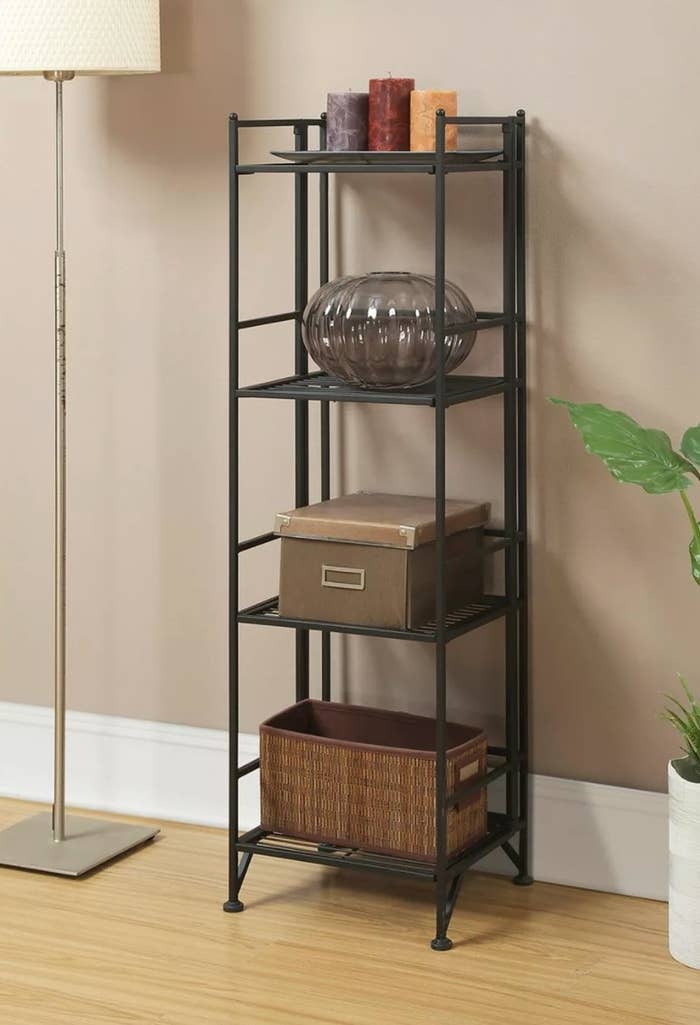 The four-tier folding metal shelf holding candles, a vase, and baskets