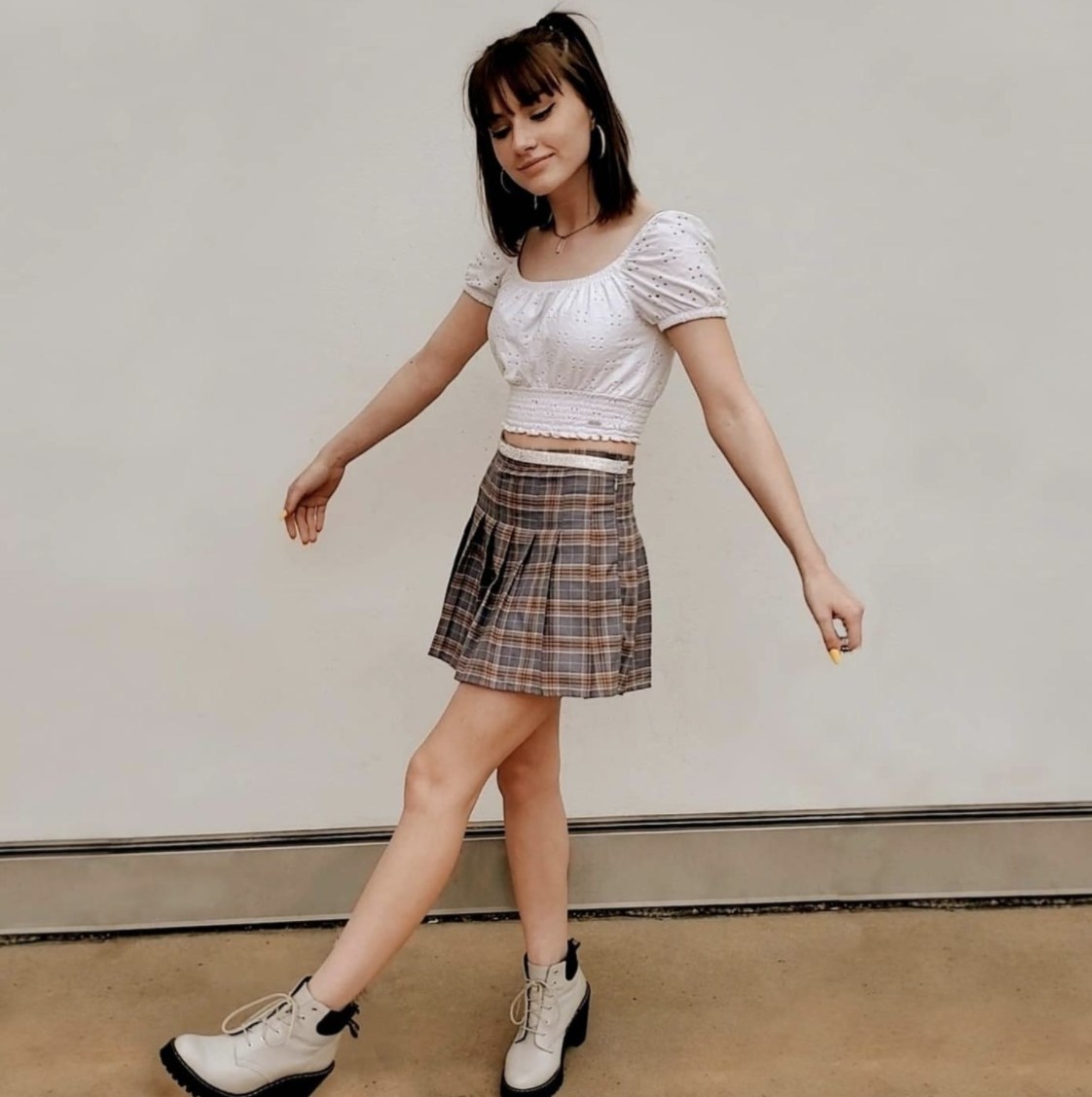 A person wearing a white top and pleated plaid skirt