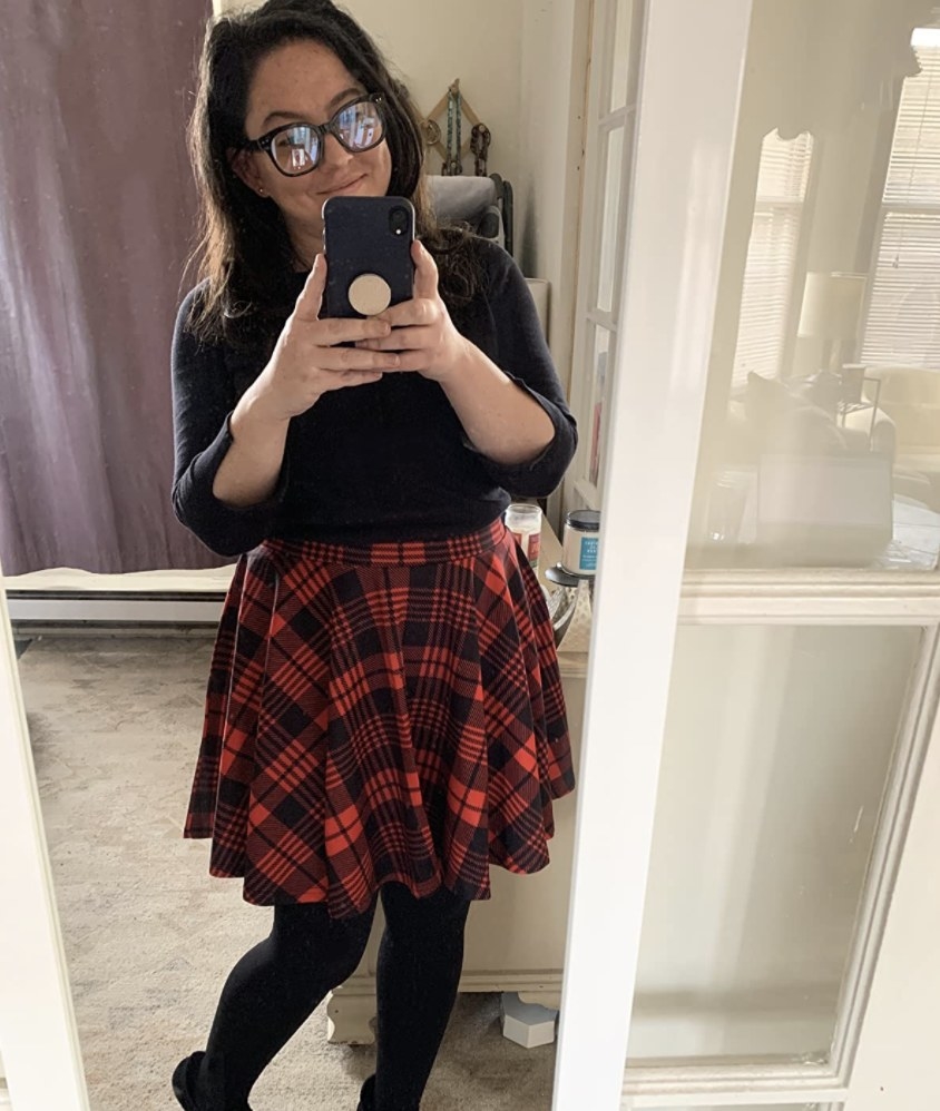 A person wearing a black top, red plaid skirt, and tights