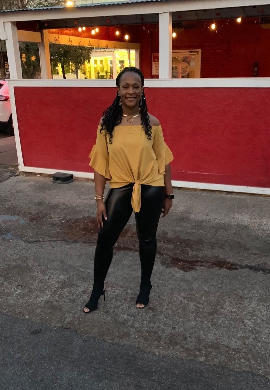 reviewer wearing the black faux leather leggings with a yellow top outside of a restaurant