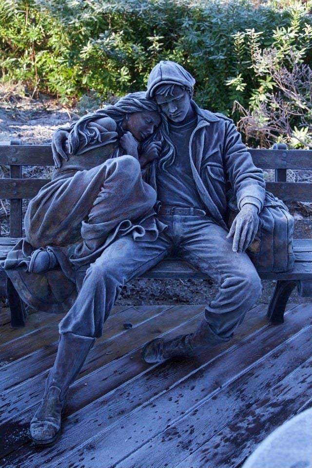 A sculpture of a man holding a woman, sitting on a bench dusted in frost that gives it coloring to look like a pencil drawing