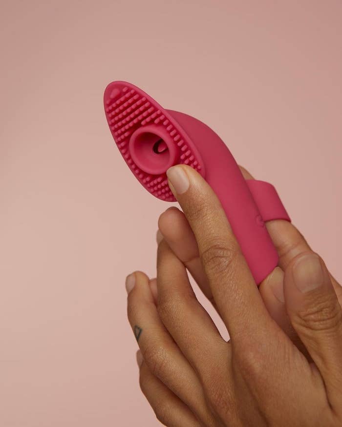 A model wearing the vibrator on their finger, with a textured paddle featuring dozens of tiny silicone rods