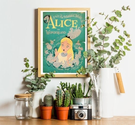 An alice in wonderland poster near some plants and knick knacks on a counter 