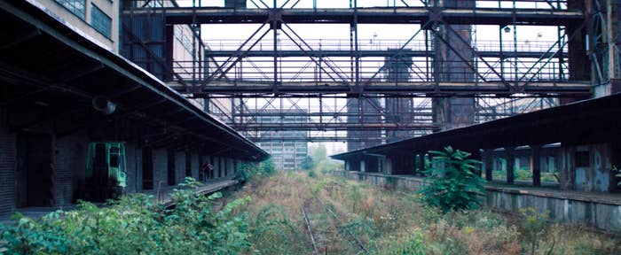 Fake Captain America running in a train station where the tracks are covered in plants