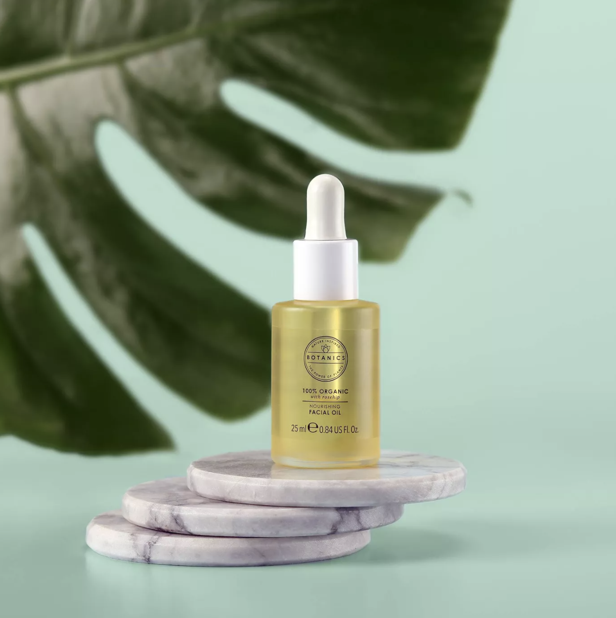 A bottle of facial oil on a coaster with a tropical leaf backdrop