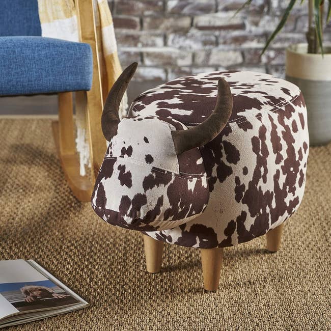 the cow-print ottoman which has four wooden legs and two upholstered horns