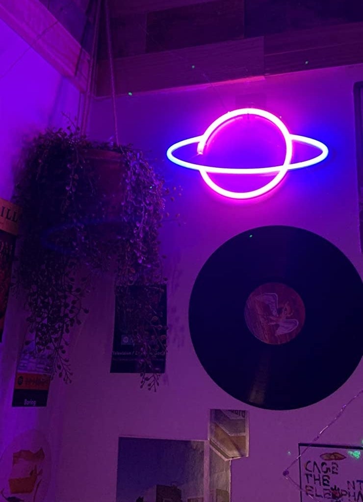 a reviewer&#x27;s neon planet hanging on the wall