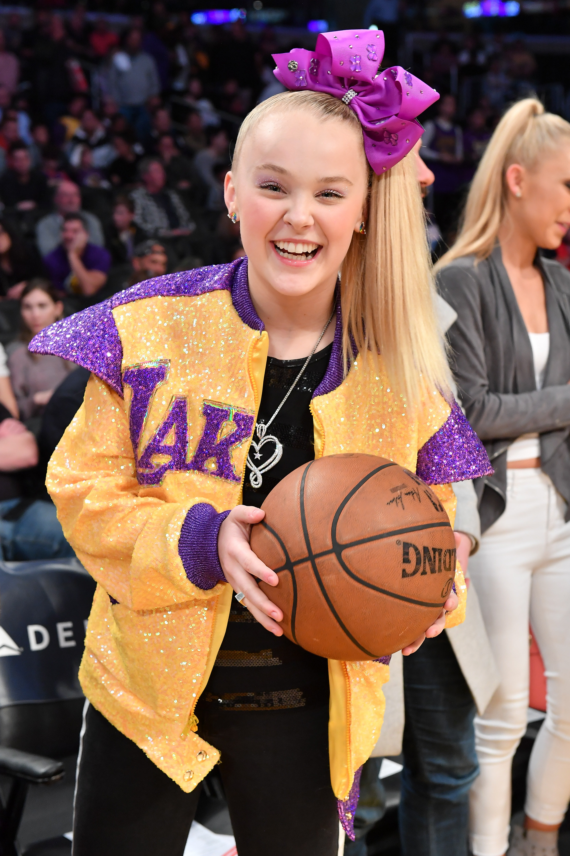 JoJo holding a basketball at a basketball game and wearing a glittered Lakers jacket