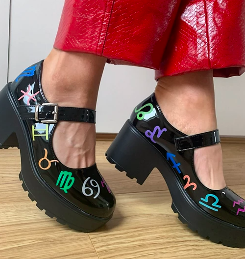model wearing black faux patent, chunky, low-heel shoes with the different horoscope signs printed all over them in bright colors