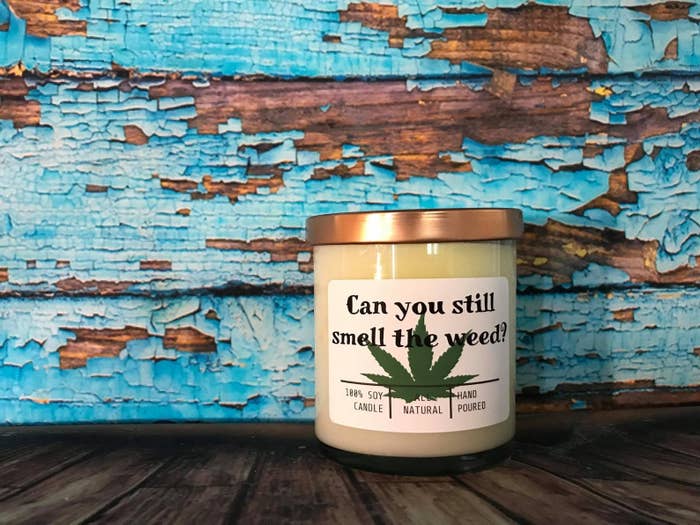 candle with gold top on it and a green marijuana leaf on the front. It says "Can You Smell The Weed?" on the label too