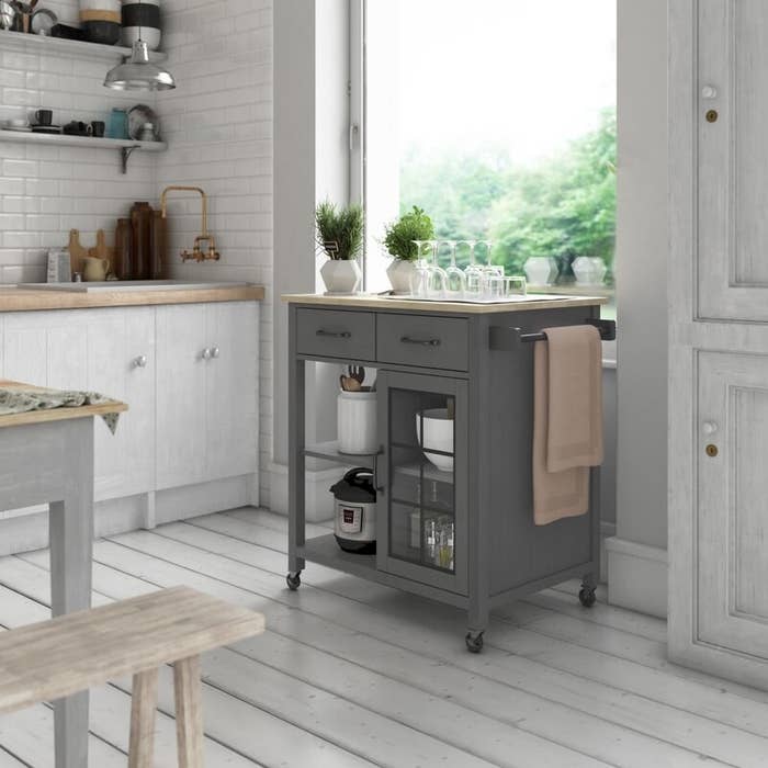 A grey, rolling kitchen cart with a wooden top, two drawers, and four shelves big enough to fit an InstantPot