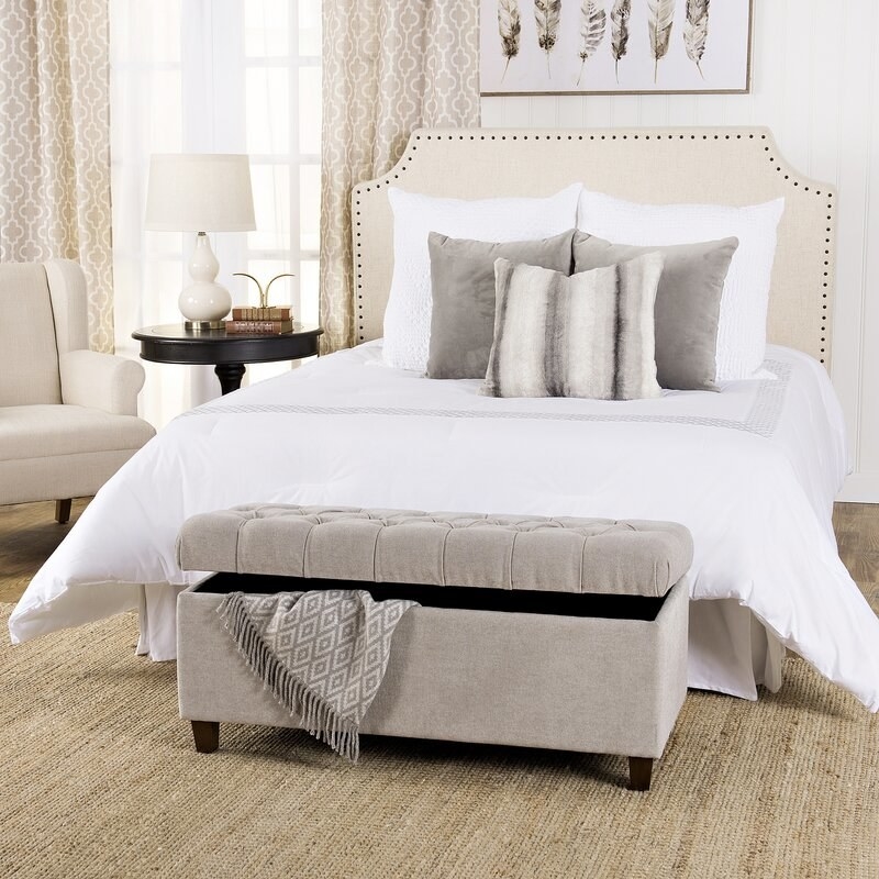 A silver ash upholstered storage bench displayed at the foot of a bed