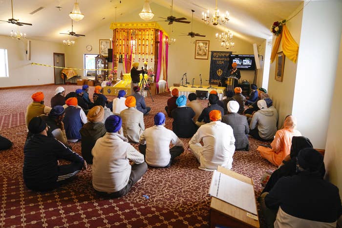 Members of the Sikh community wearing colorful dastār sit on the floor of a satsang listening to a speaker