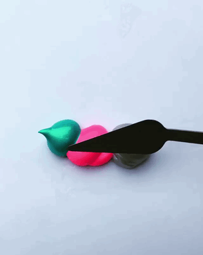 A GIF of metallic green, pink and silver paint being spread by a palette knife.