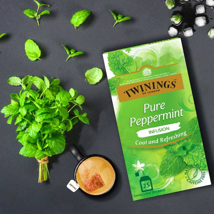 The box of the tea. A cup of peppermint tea and mint leaves are kept next to it.