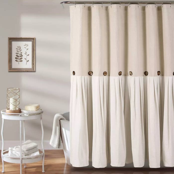 The beige curtain hanging over a bathtub with a side table next to it
