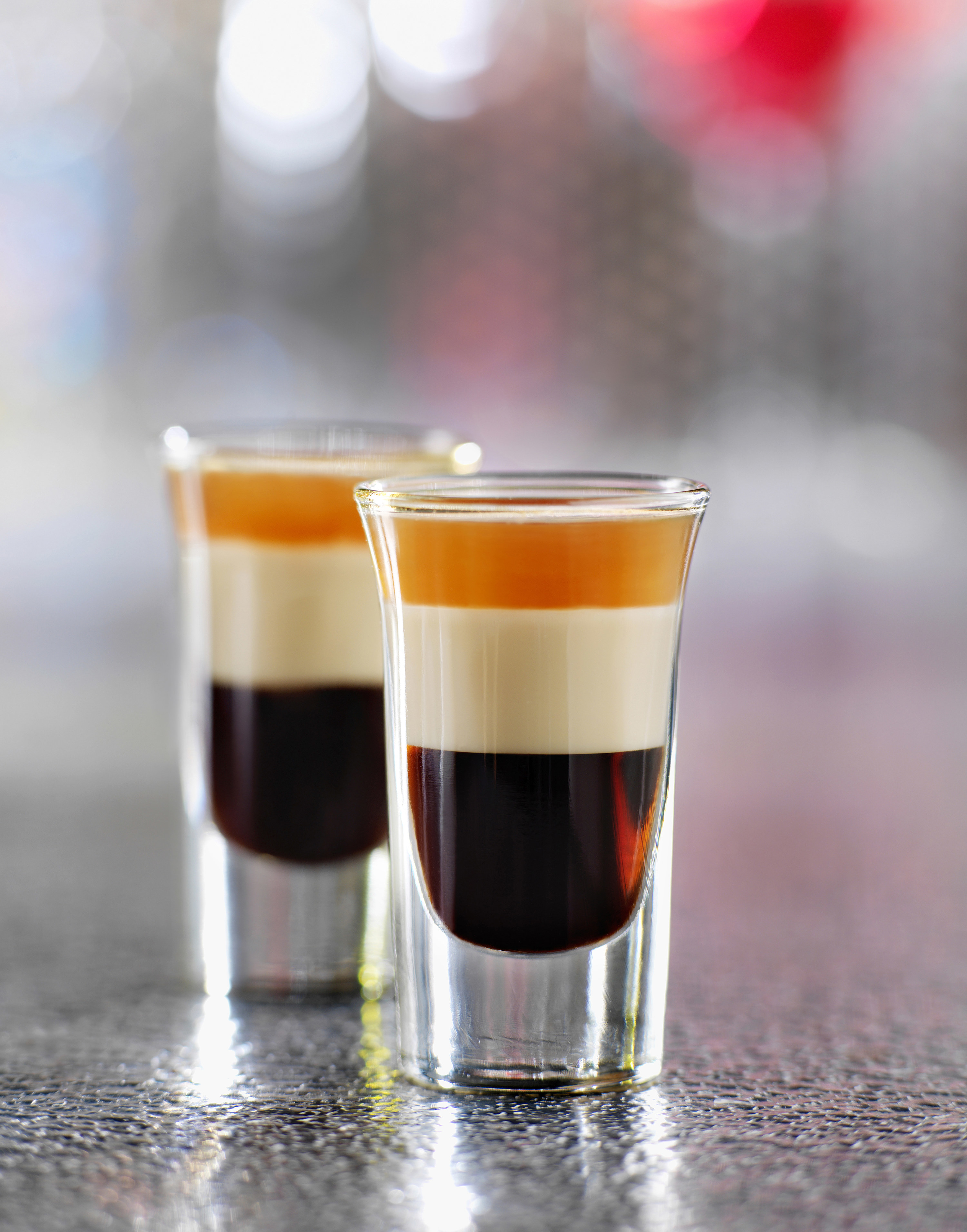 Two shot glasses with filled three layers of (from top) orange, white, and translucent dark red liquor. 