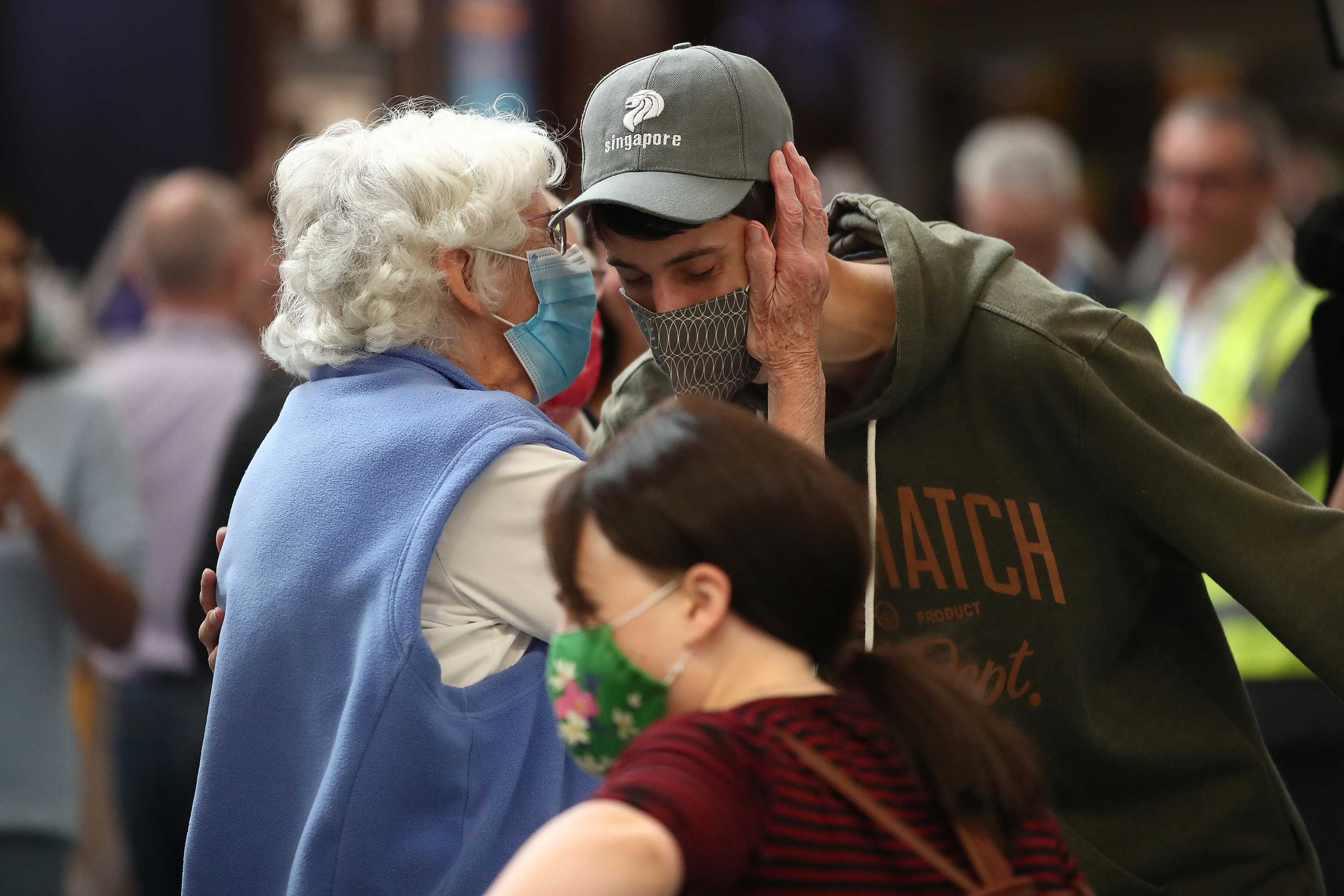 An elderly woman leans in to hug a young person