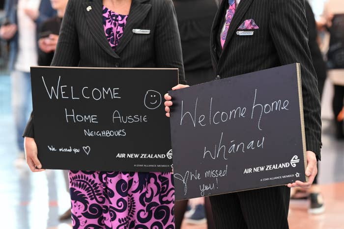 People holding signs that sat "Welcome Home Aussie" and "Welcome home Whānau"