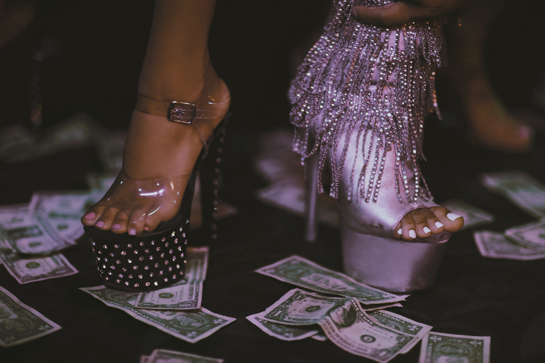 Two women in very high-heeled shoes walking on a floor littered with money