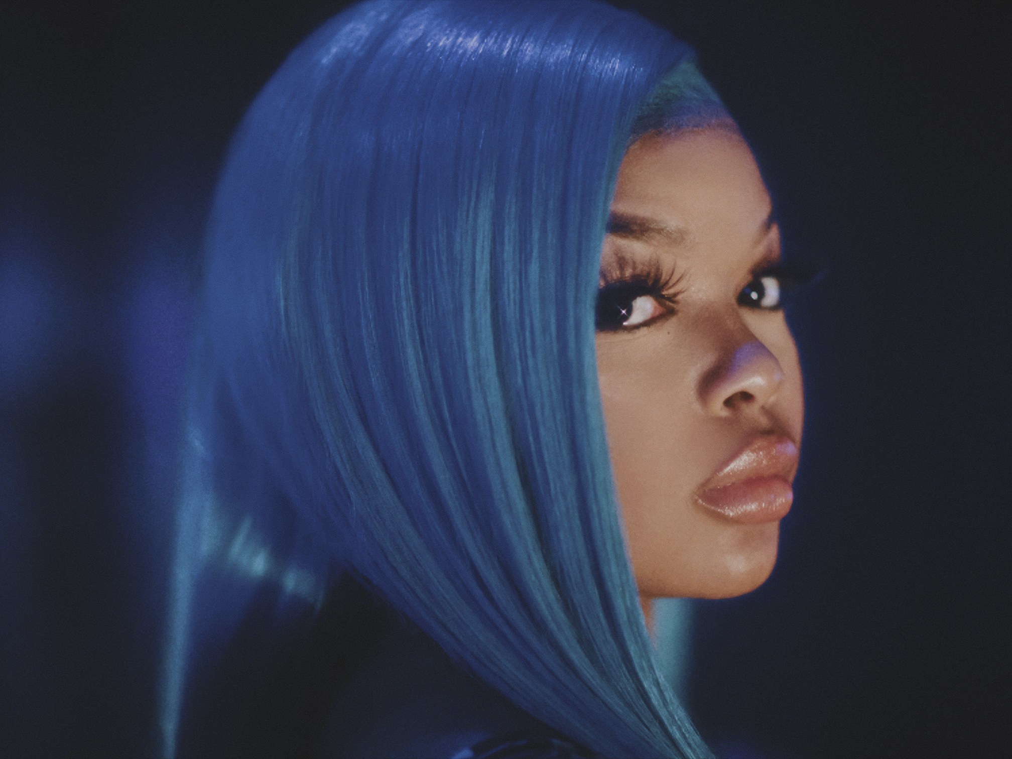 A dancer in a blue wig looks past the camera