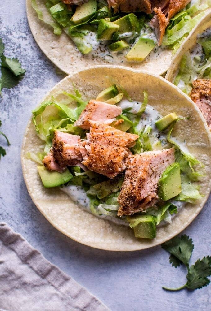 A taco topped with flaky salmon, avocado, lettuce, and creamy sauce.