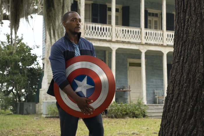 Sam holding the shield in front of a house