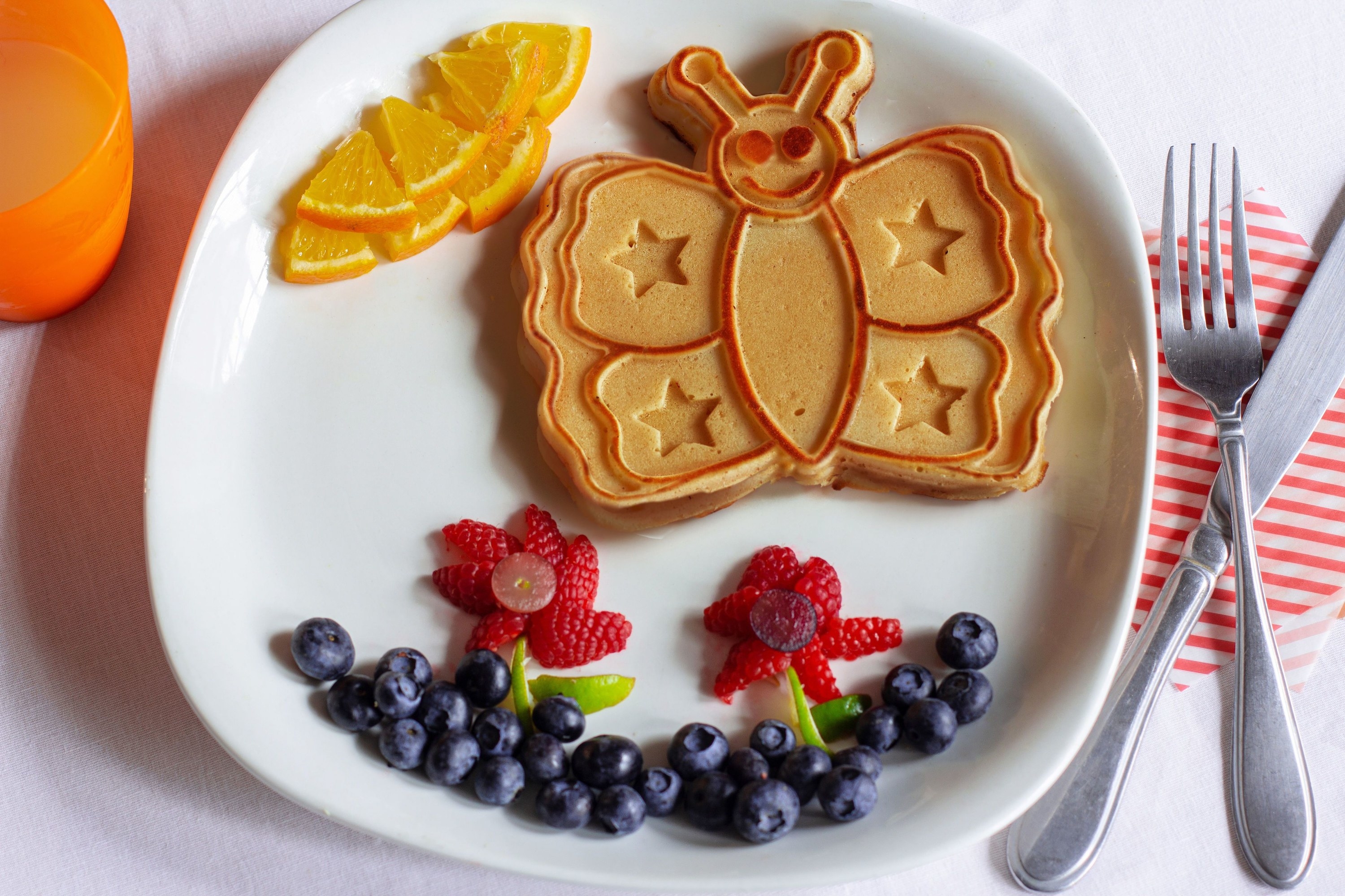 A butterfly-shaped pancake on a plate with fresh fruit