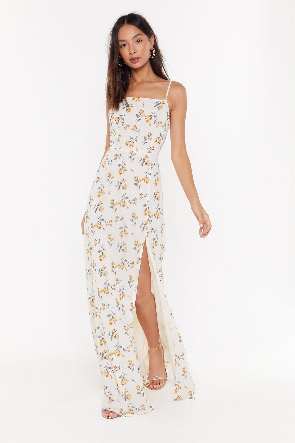 A person wearing a maxi floral dress with a box neck and slit up one leg 