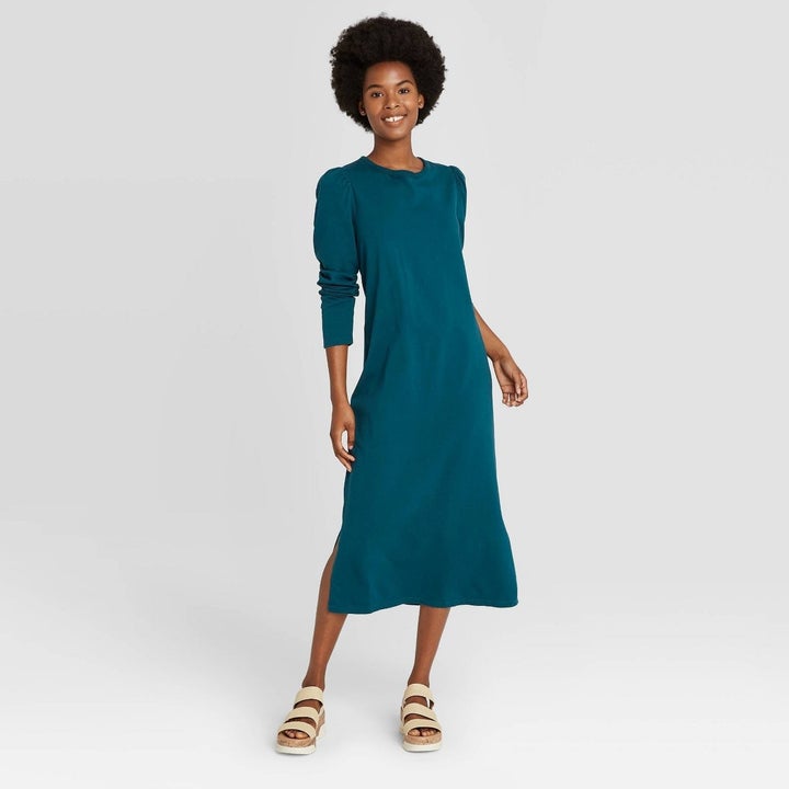 Model wearing blue dark turquoise dress with puff sleeves, goes past the knees