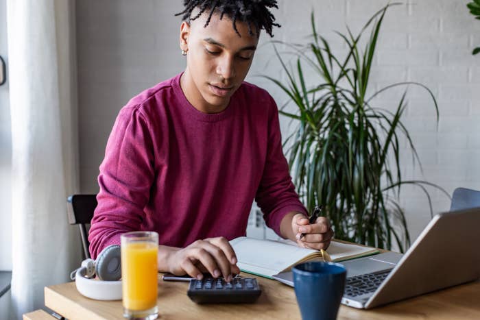 Person making a budget with a calculator, pad of paper, and laptop