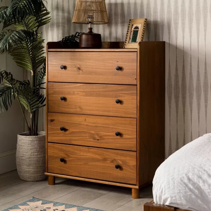 The caramel-colored dresser with black knobs