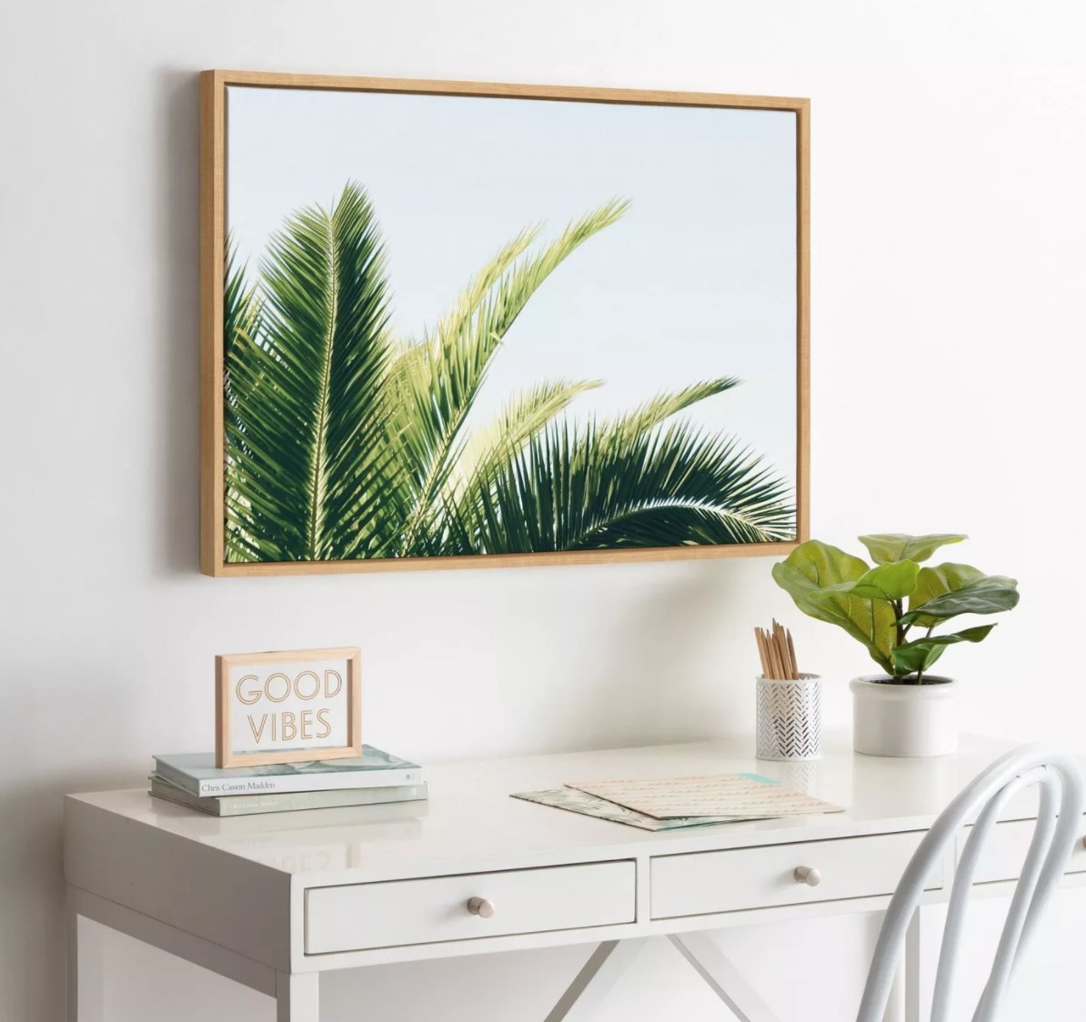 The picture of a tropical palm in a wood frame hung above a white desk